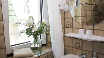 Een badkamer met een wastafel, spiegel, handdoekhouder en een vaas met bloemen.