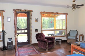 A cozy living room with a wooden door, a rocking chair, a small table, and a ceiling fan.