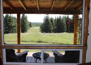 A wooden deck with two tables and chairs, overlooking a grassy field and forest.