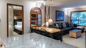 A modern living room with a dining area, a fireplace, and a large window with a view. - Aspens #219 Prime Ski-in Ski-out Location! Pool, Hot tubs, BBQ, sleeps 8 (Whistler)