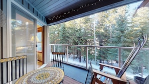 Enjoy a serene forest view from this balcony with a tiled floor, wooden table, and bench.