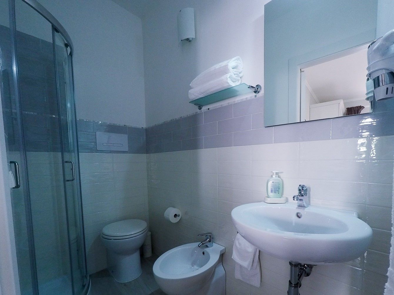 Ein Badezimmer mit Duschkabine, Toilette, Bidet und Waschbecken mit Spiegel darüber.