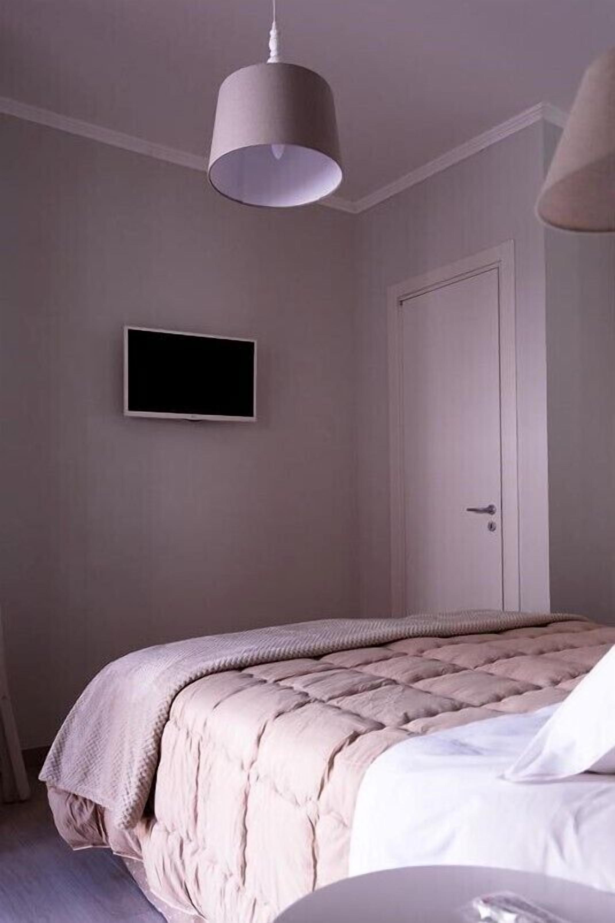 A bedroom with a bed, a television mounted on the wall, and a door.