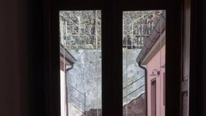 Une porte donnant sur un escalier en pierre avec une rampe en métal, un pot de fleurs et un bâtiment à la façade rose.