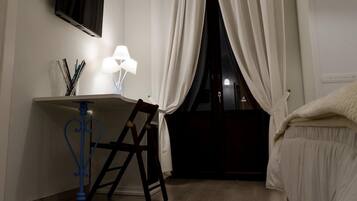 A bedroom with a bed, a desk with a chair, a TV mounted on the wall, and a window with curtains.