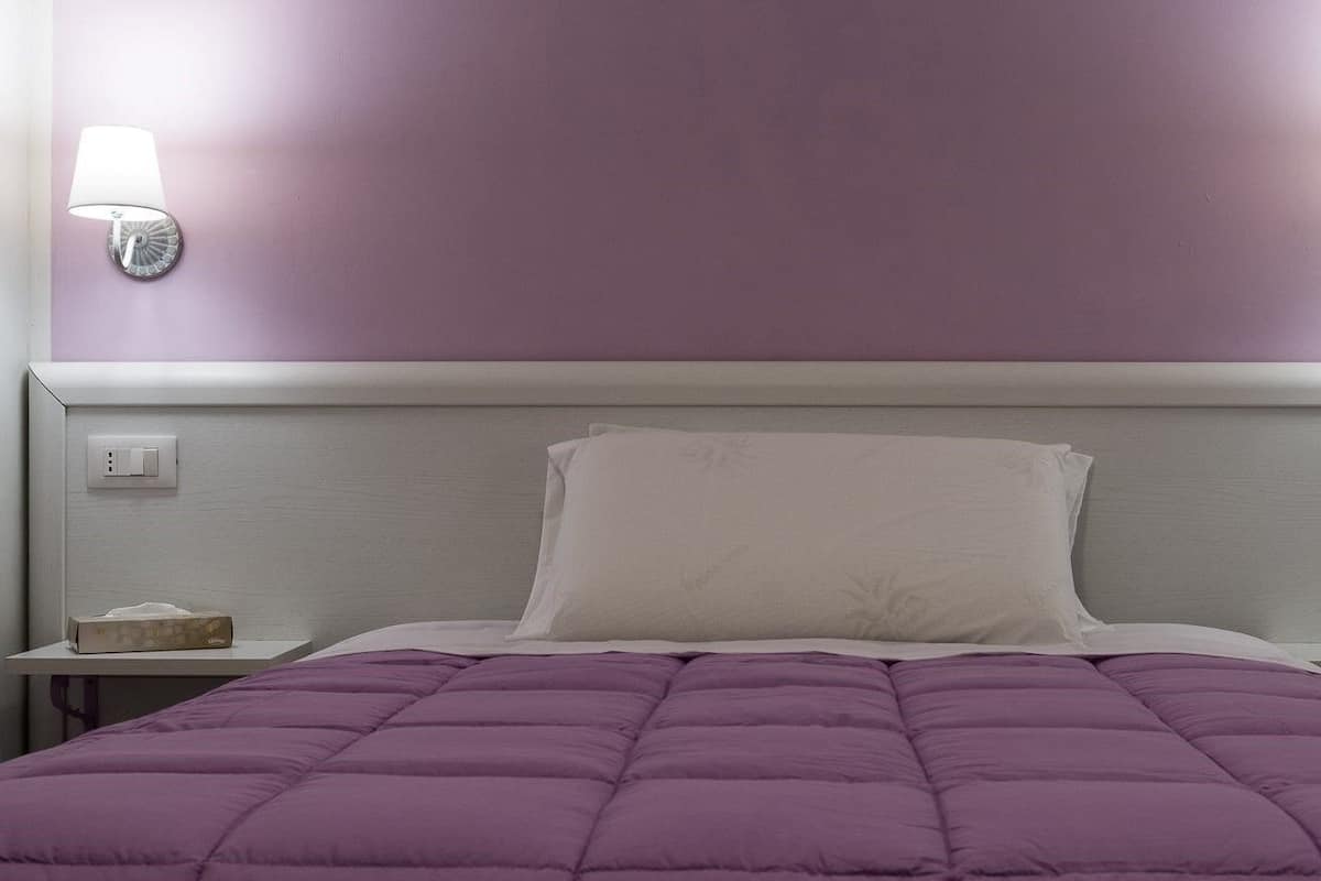 A hotel room with a bed, a nightstand, a lamp, and a tissue box.