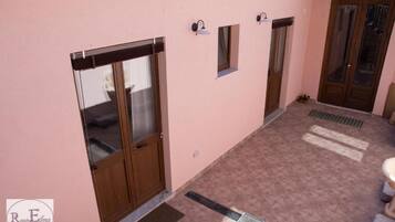 Un pasillo con pared rosa, una puerta de madera, un ventanal pequeño y una lámpara.
