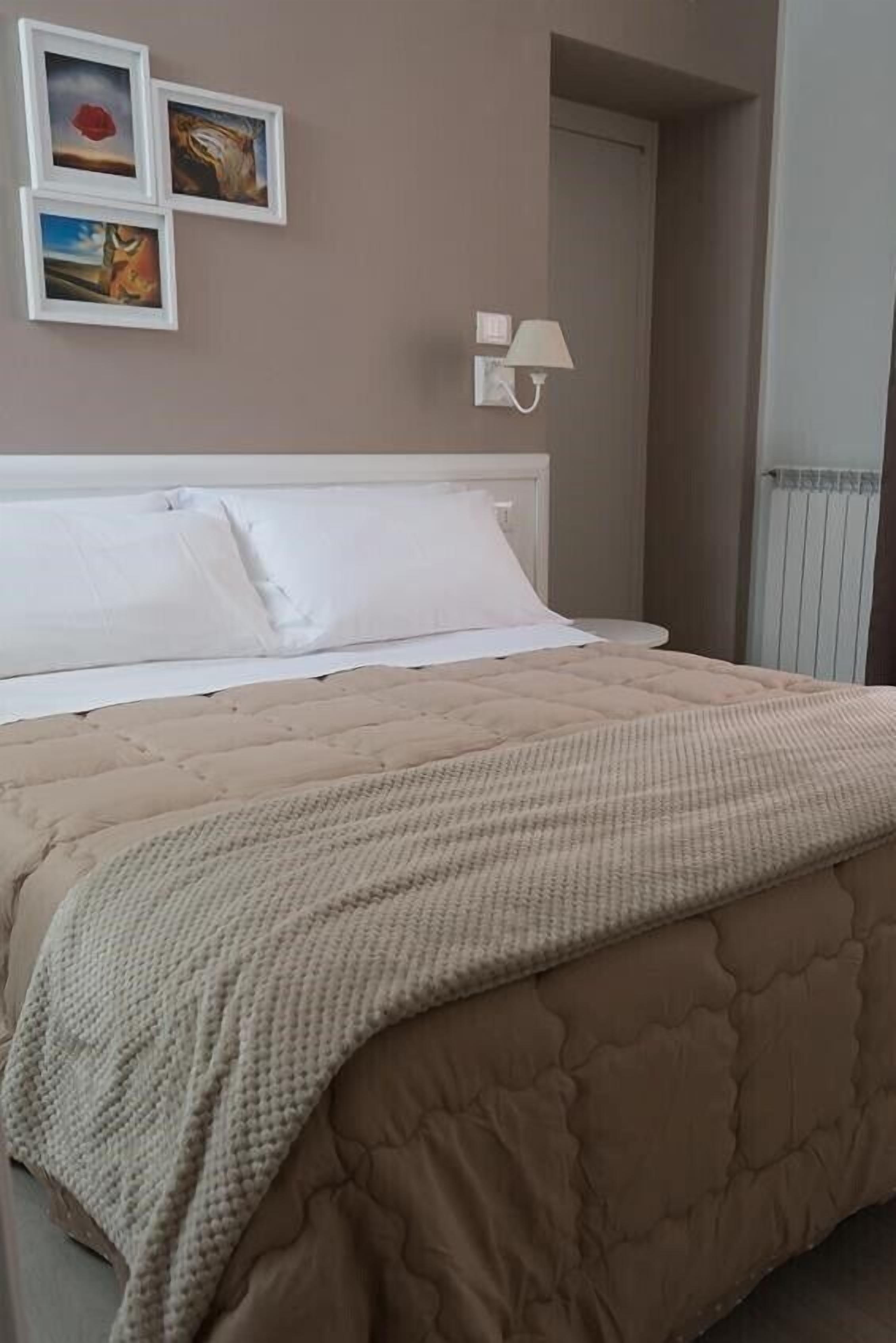 Une chambre à coucher avec un lit, une tête de lit blanche, une couvre-lit matelassée beige et trois tableaux encadrés accrochés au mur.