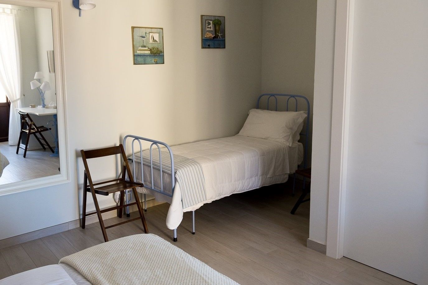 A small, single-bed room with a wooden chair, a desk, and two wall-mounted pictures.