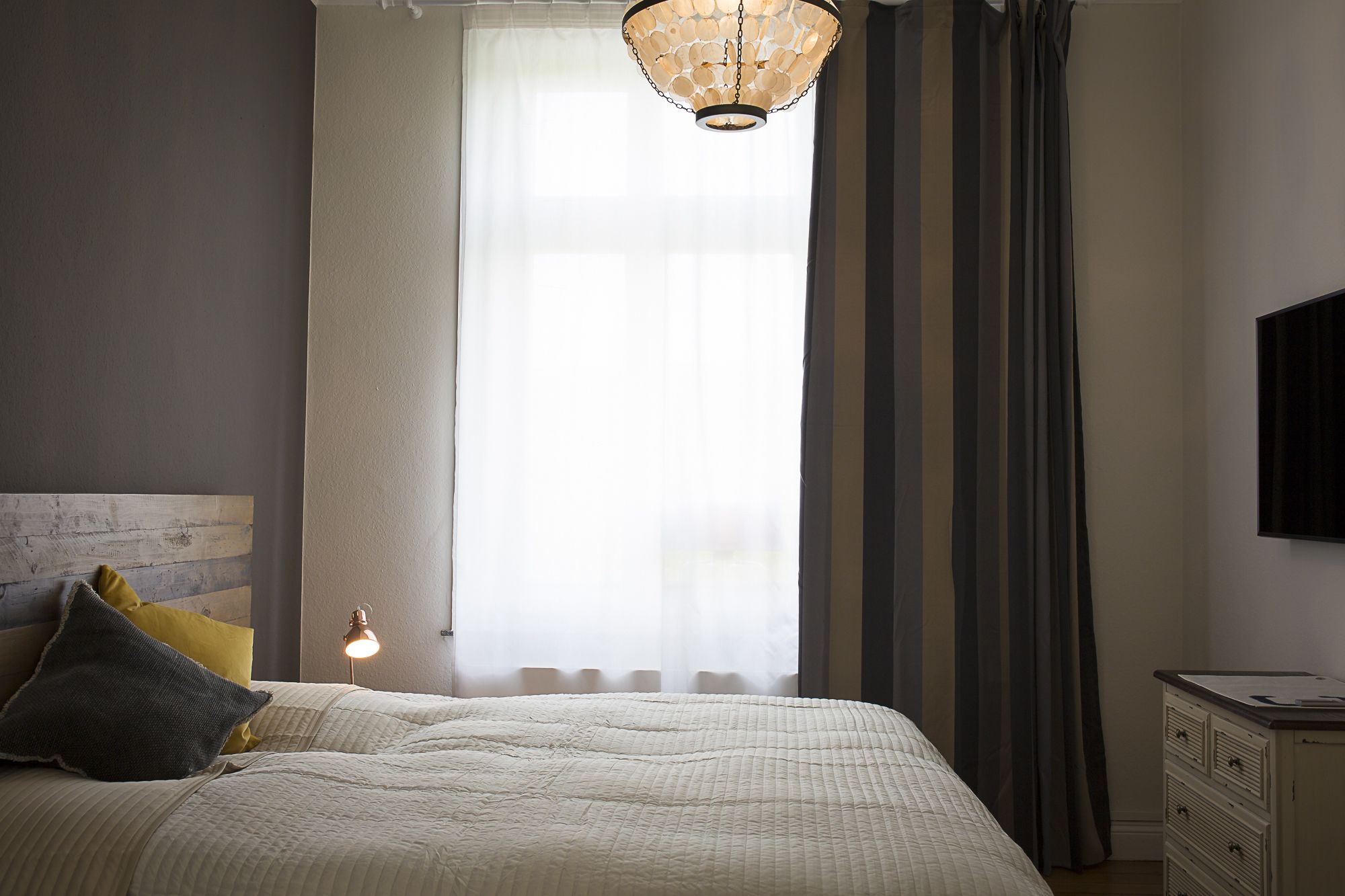 A bedroom with a bed, a bedside lamp, a dresser, and a TV on the wall.