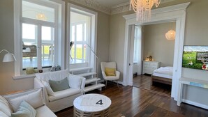Un salon spacieux doté d’une grande fenêtre, d’un lustre et d’un coin salon confortable.