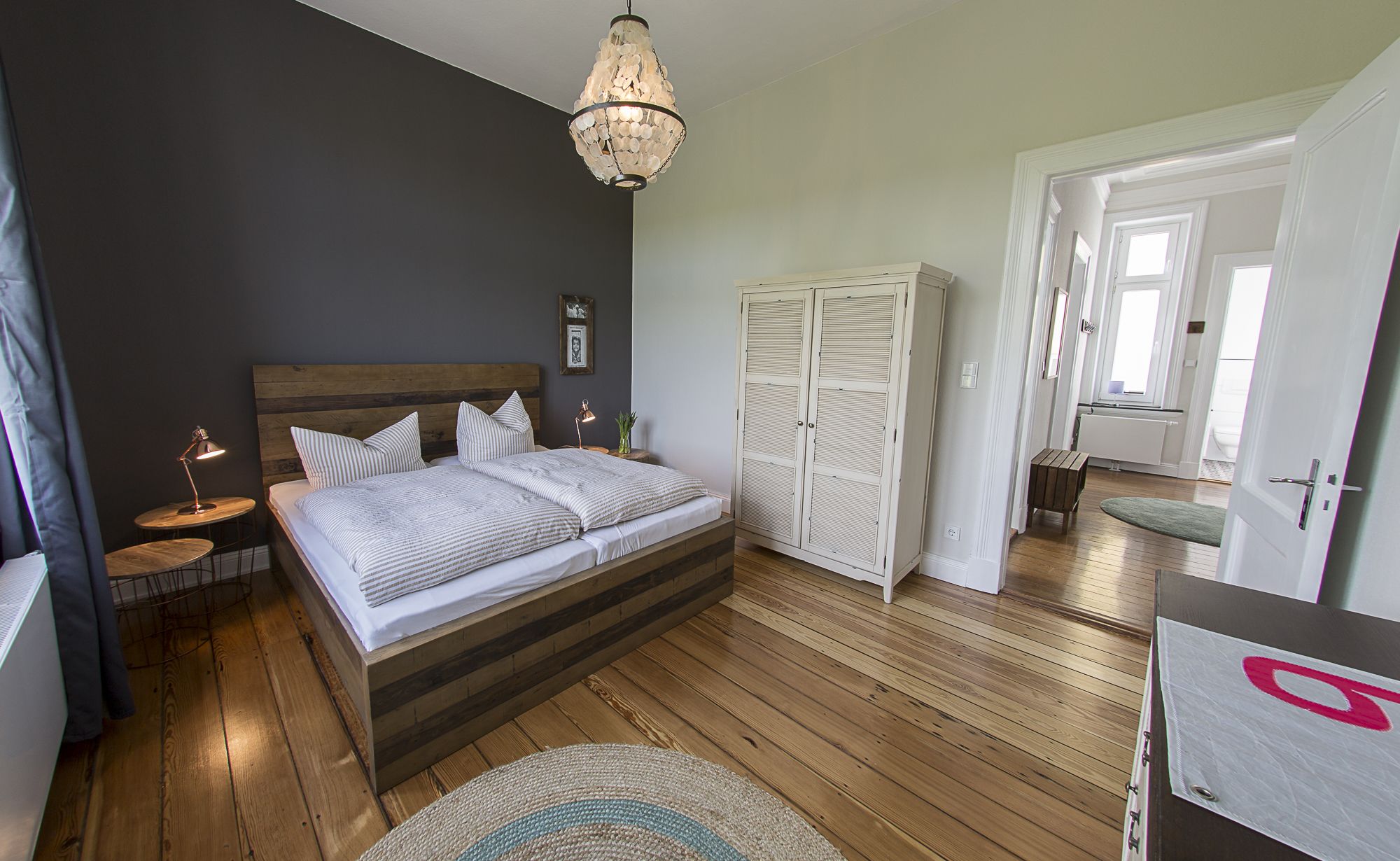 A bedroom with a wooden bed, bedside tables, a chandelier, and a wardrobe.