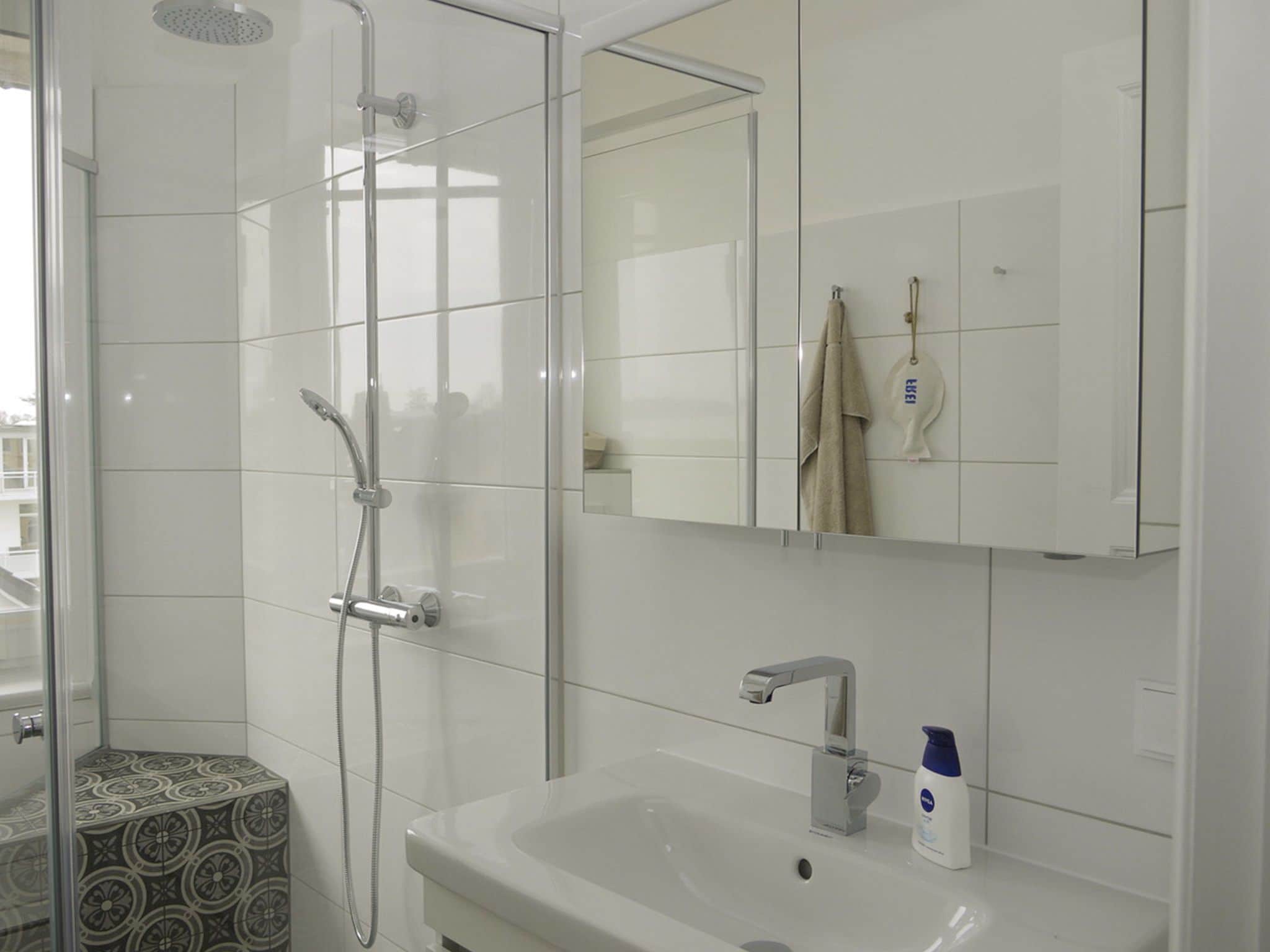 Un baño moderno con ducha de vidrio, un lavabo blanco con un solo grifo y un espejo sobre el lavabo.