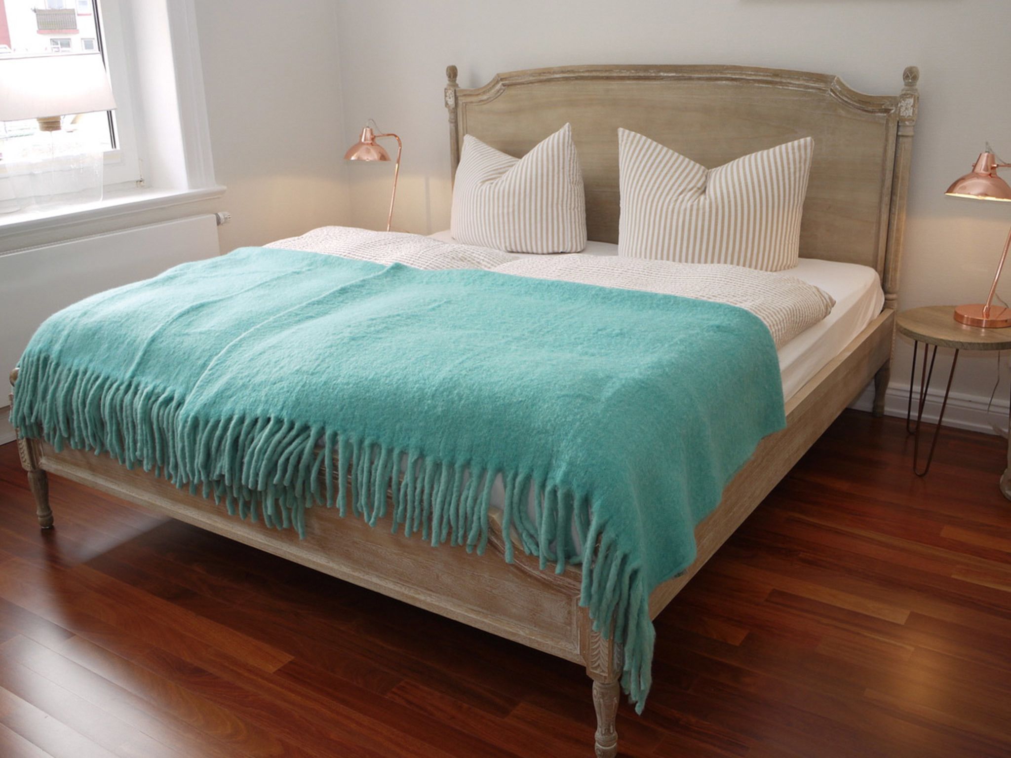 Ein Bett mit einer türkisblauen Decke, einem Holzkopfteil und zwei Nachttischlampen.