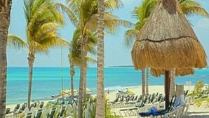 Eine Strandansicht mit Palmen, einer umbauten Hütte und Liegestühlen.