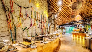 Ein Buffetbereich mit verschiedenen Speiseauslagen und einer Steinwand mit bunten Seilen.
