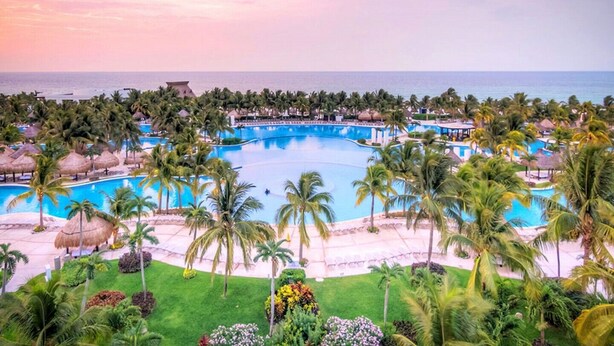 Ein Resort mit einem großen zentralen Pool, umgeben von Palmen und einem Strandabschnitt.
