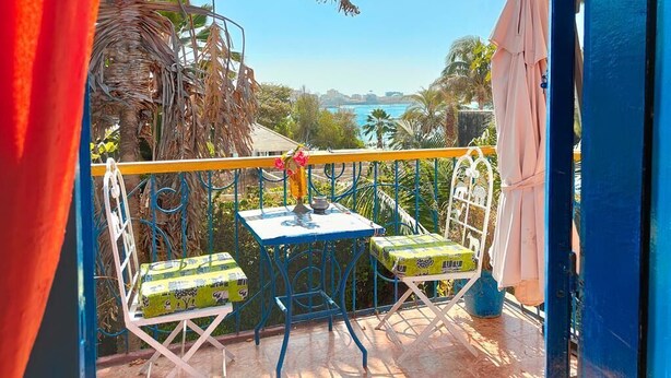 Un balcon avec une table et des chaises, une vue sur la mer et un palmier.