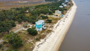 An aerial view of a coastal property with a beach, a large house with a blue roof, and a smaller building with a white roof. - Ocean Springs 'Magnolia Beach House' on Pvt Beach! (Ocean Springs)