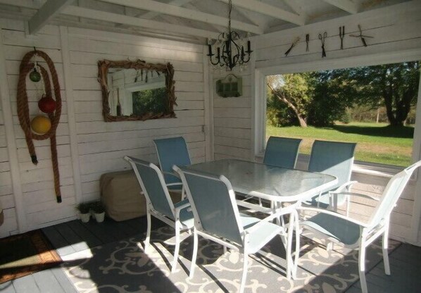 Une terrasse couverte avec une table et des chaises, un lustre et une vue sur l’extérieur.
