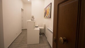 A hallway with a reception desk, a chair, a radiator, and a door with a painting on the wall.
