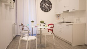 A modern kitchen with white cabinets, a round coffee-themed wall art, and a dining area with a white table and chairs.
