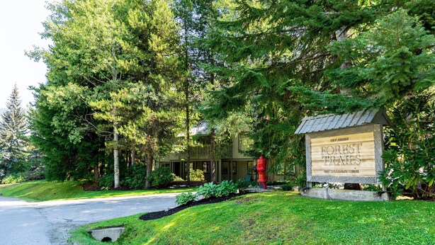 A building with a sign for Forest Trails, surrounded by lush greenery and trees.