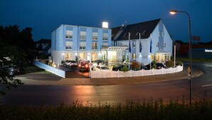 Een hotel met een witte gevel, veel ramen en een hekwerk.