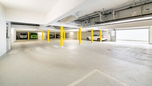 Een parkeergarage met meerdere verdiepingen, gele pilaren, betonnen vloeren en verlichting aan het plafond.