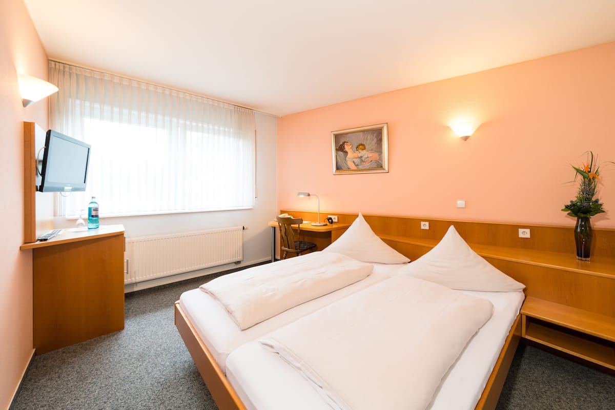 A hotel room with a bed, a desk, a chair, a television, and a window with curtains.