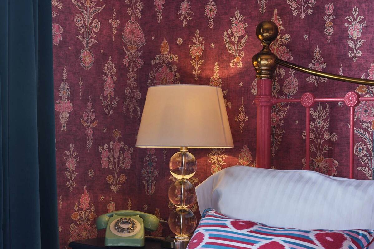 A bed with a striped pillow, a vintage-style lamp, and a rotary phone on a nightstand.