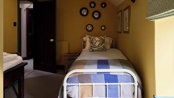 Un dormitorio con cama, mesita de noche, radiador y una pared con espejos circulares y cuadros enmarcados.