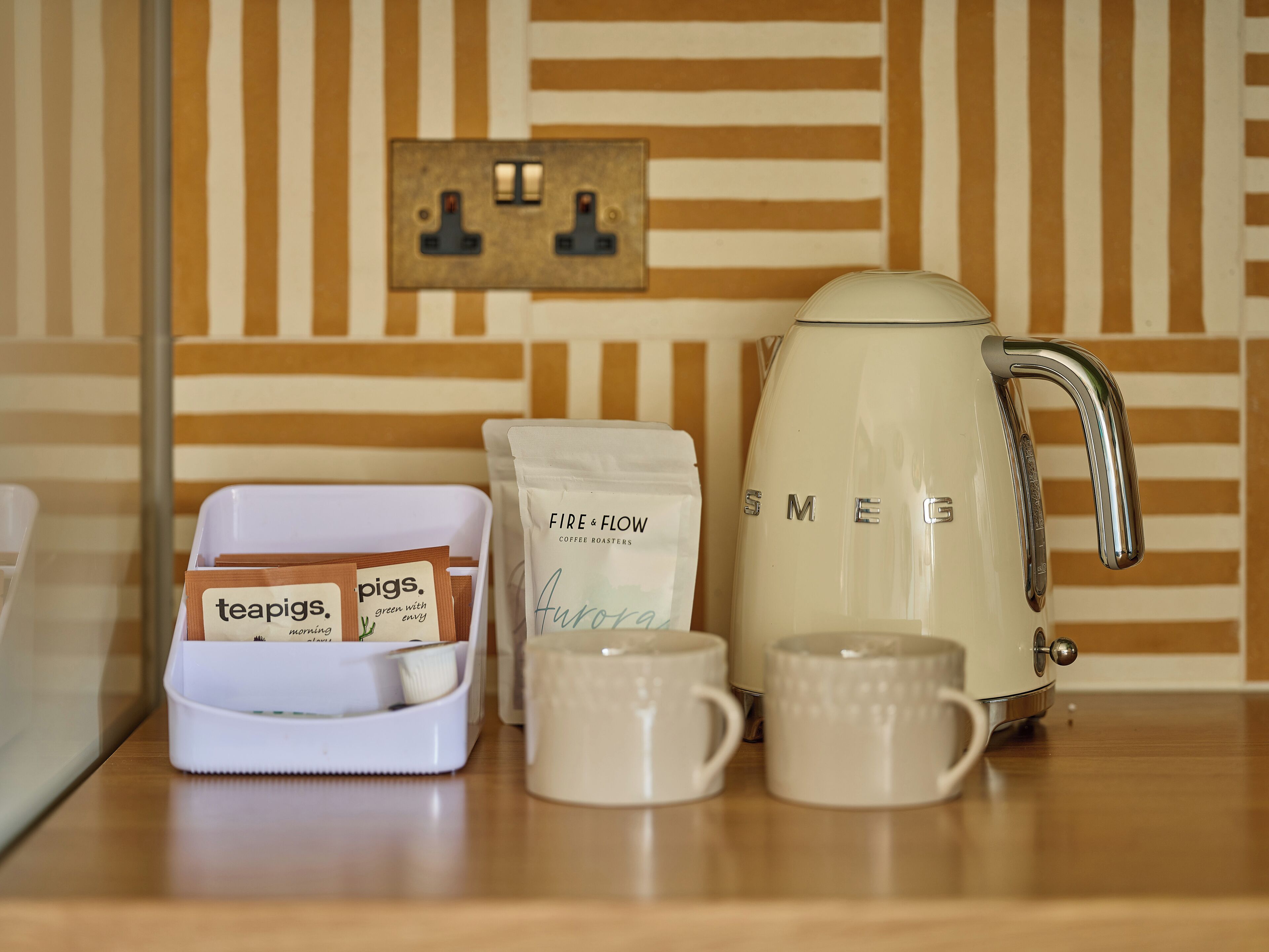 A kitchen counter with a coffee maker, two mugs, a teapot, and a tray with tea bags and coffee pods.