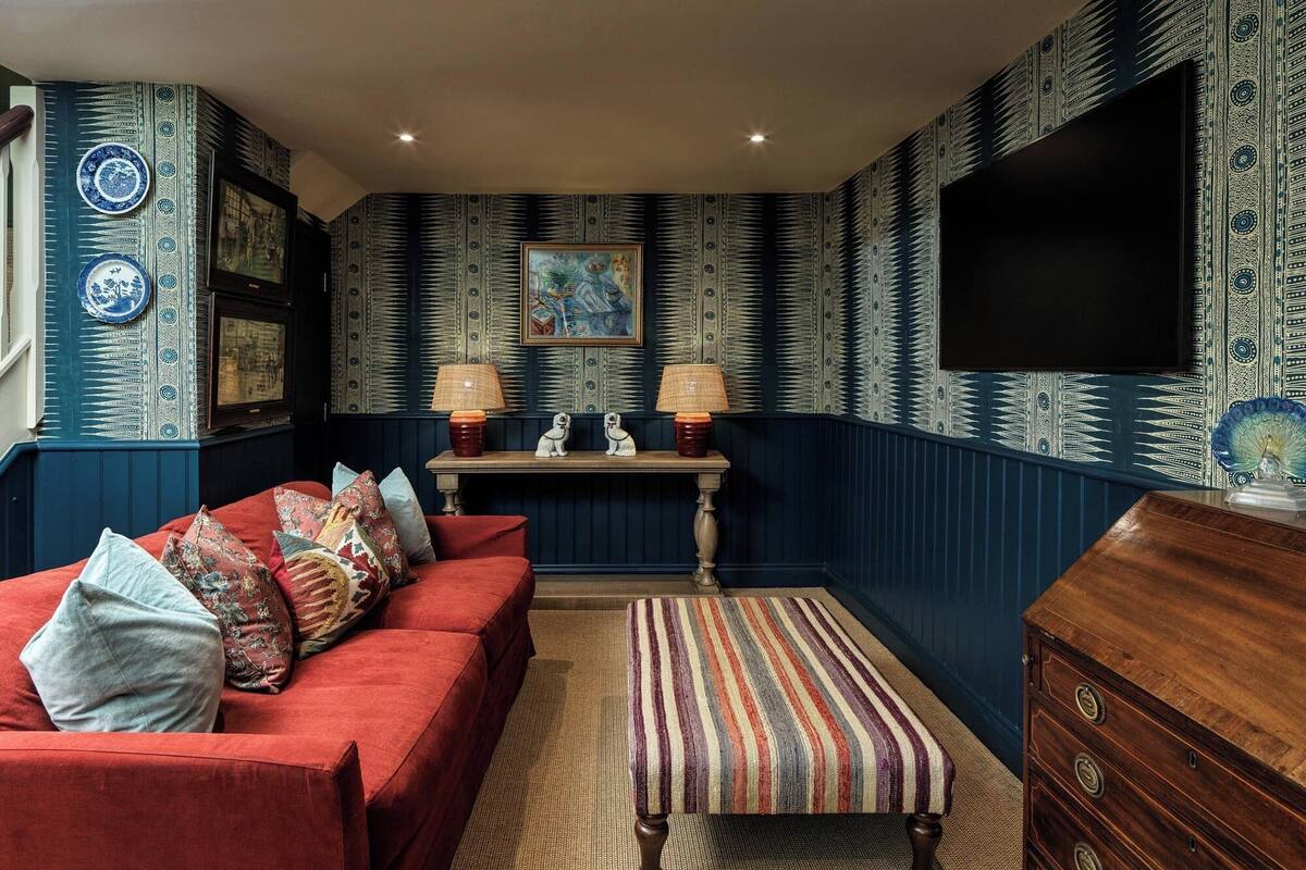 A room with a red sofa, patterned wallpaper, a wooden dresser, and a television mounted on the wall.
