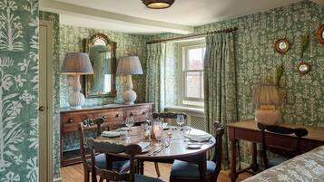 Comedor con una mesa de madera dispuesta para cuatro personas, rodeada de sillas tapizadas. Un aparador de madera con espejo y lámparas está contra la pared.