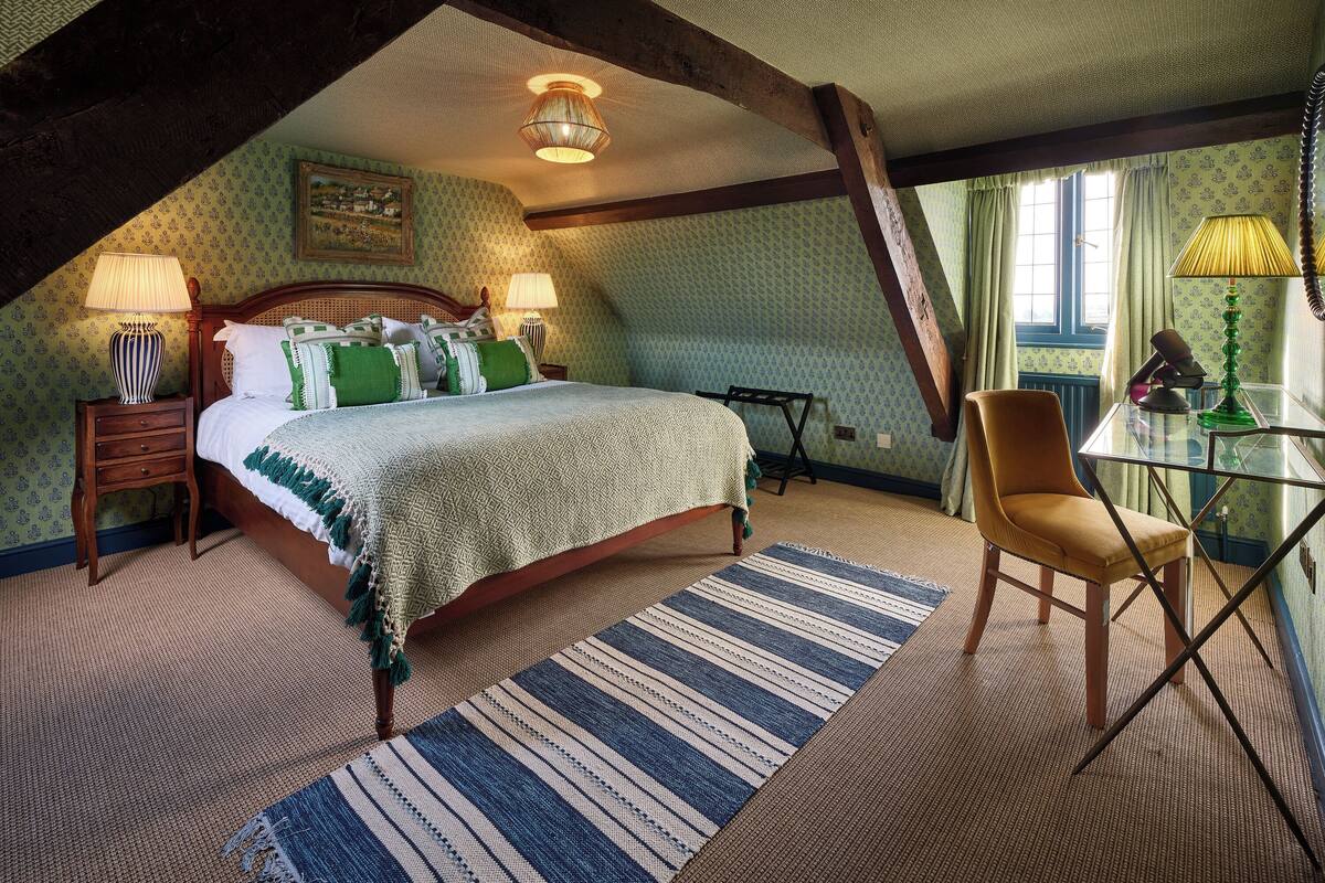 A bedroom with a bed, two bedside lamps, a chair, a table, and a window with curtains.