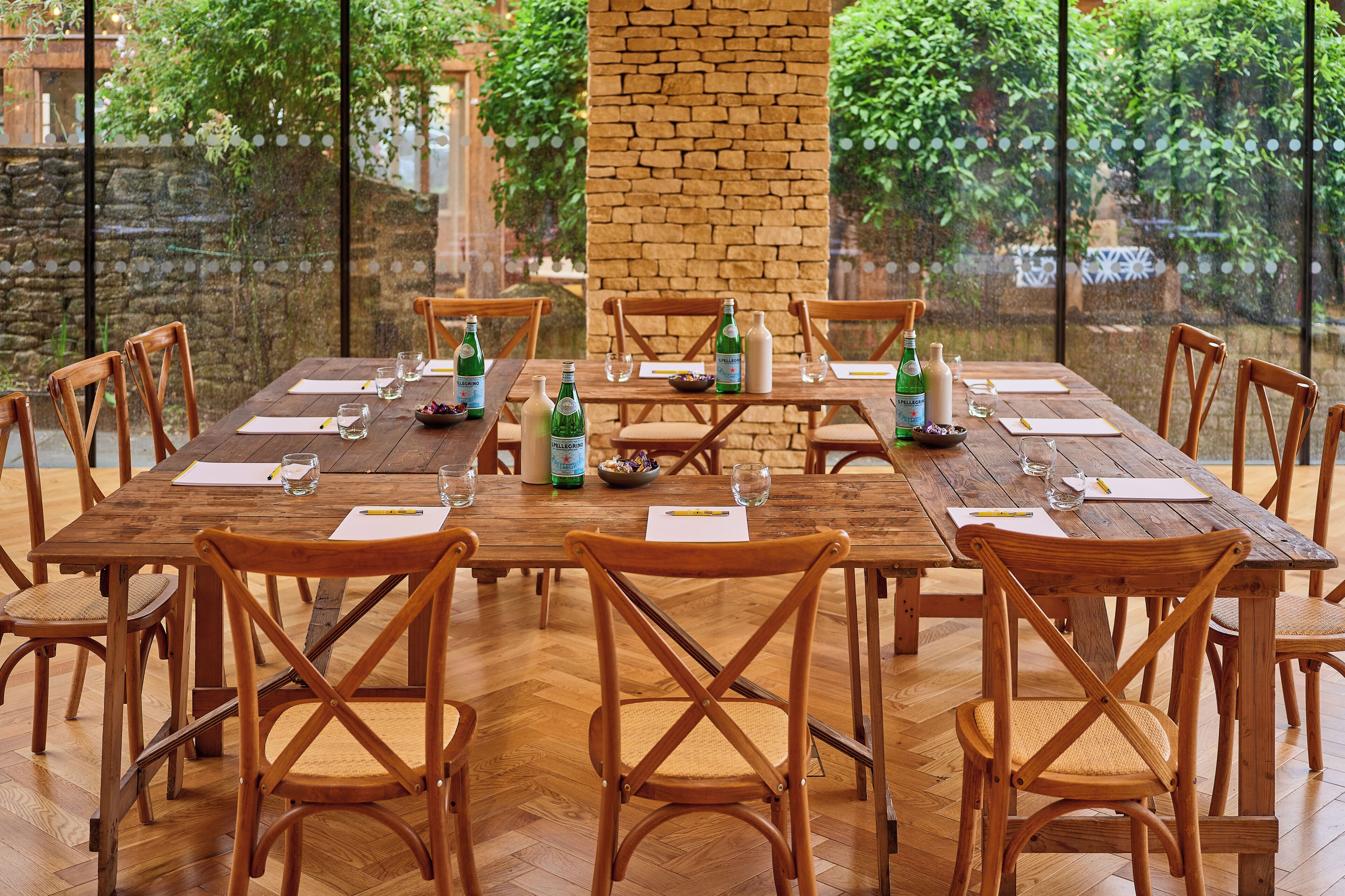 Una mesa de comedor de madera dispuesta con sillas, botellas, vasos y una vela.