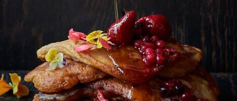 A stack of pancakes with syrup being poured over them, garnished with berries and flowers.
