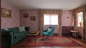 En stue med en grøn sofa, en turkis lænestol, et mønstret tæppe og et vindue med gardiner.