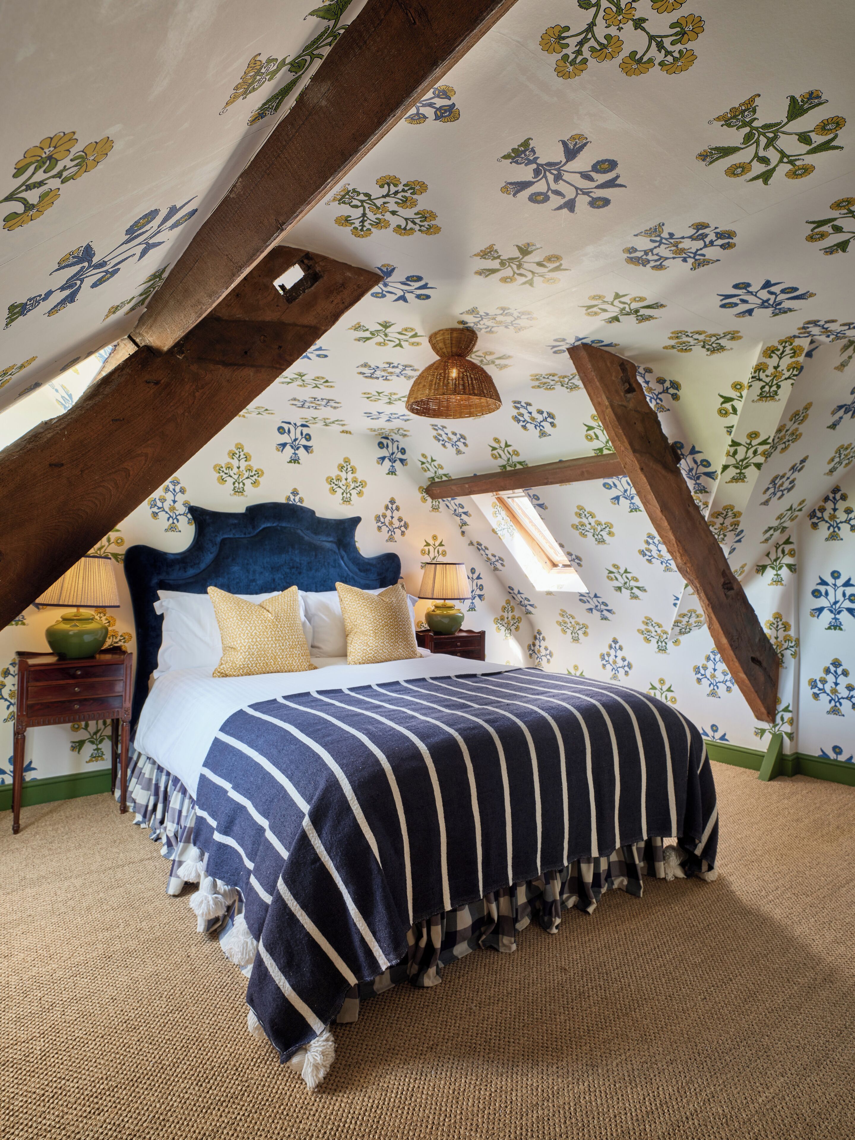 A bedroom with a sloped ceiling, a bed with striped bedding, and floral wallpaper.