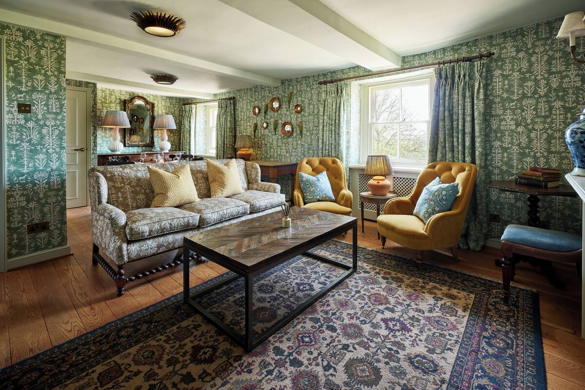 A traditional living room with patterned wallpaper, a sofa, armchairs, a coffee table, and a rug.