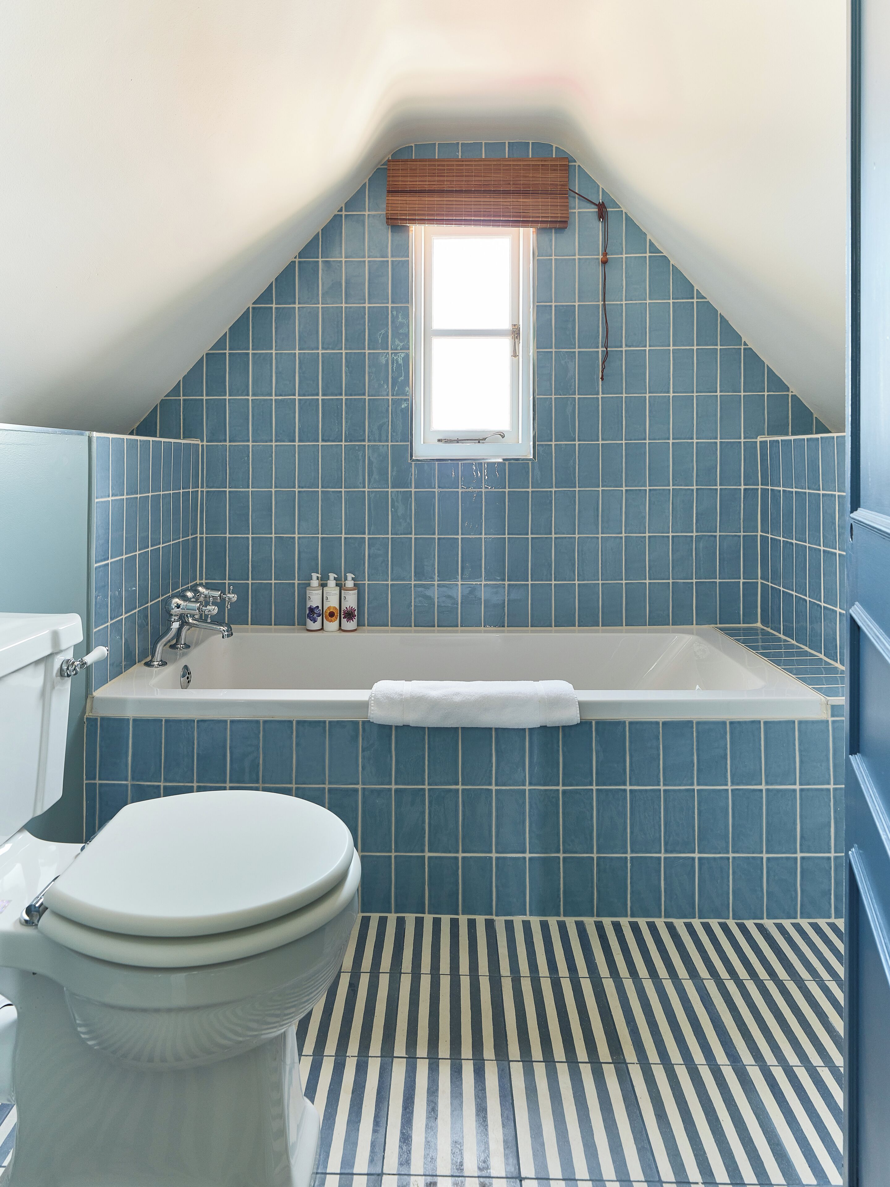 A bathroom with a bathtub, toilet, and a window with a wooden blind.