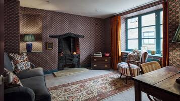 A traditional room with patterned wallpaper, a fireplace, a sofa, a chair, and a window with curtains.