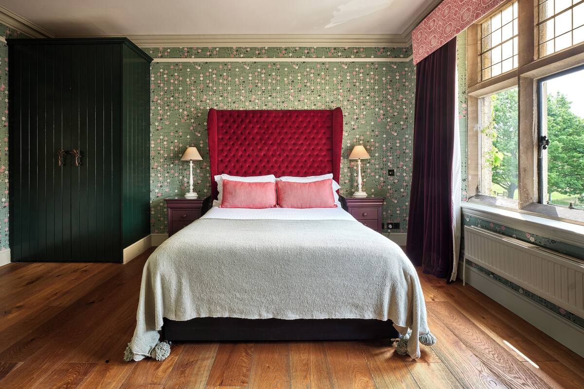 A bedroom with a large bed, green wallpaper, and a view through a window.