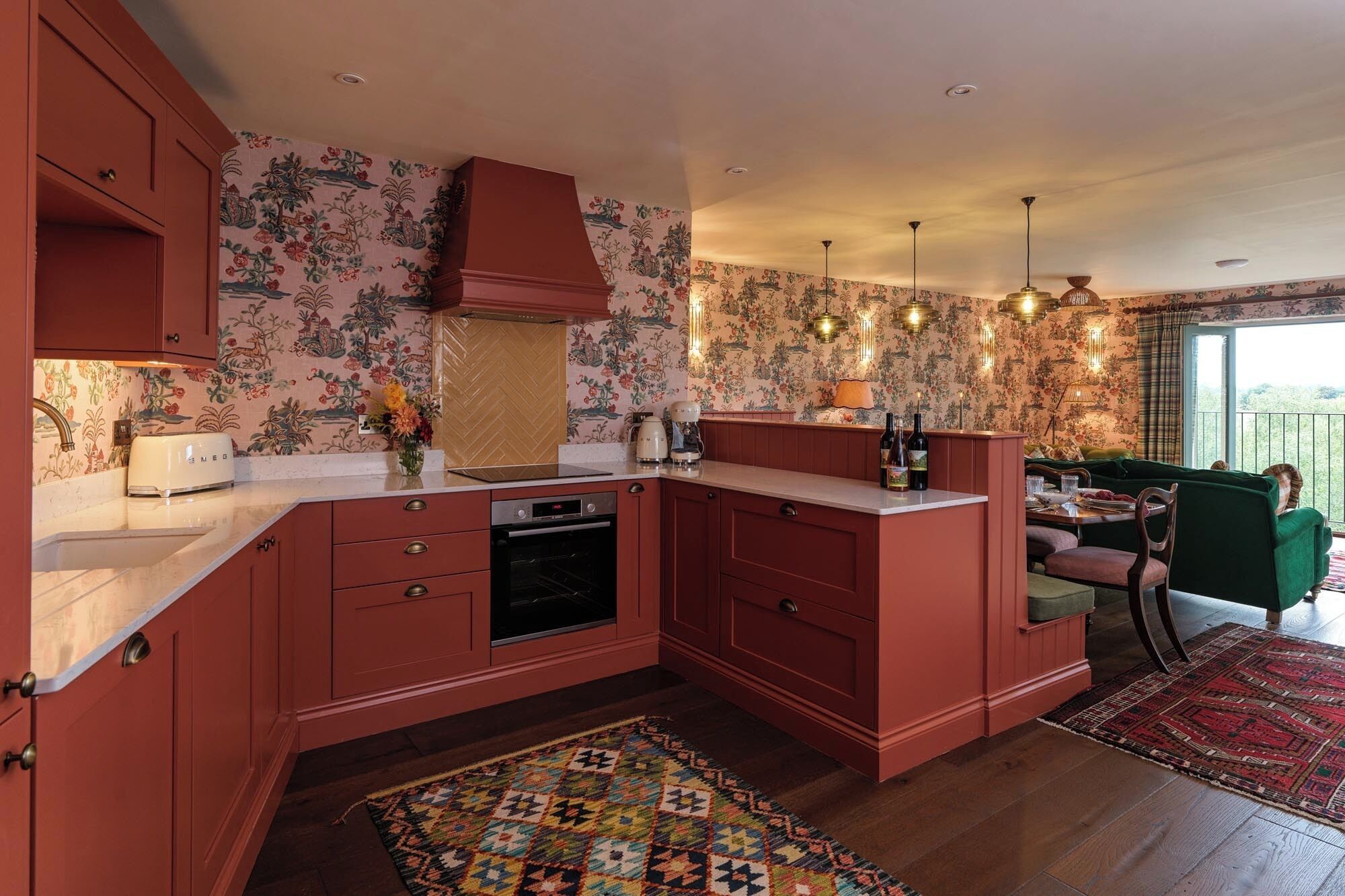 A kitchen with a built-in oven, a sink, and a dining area with a green sofa and a patterned rug.