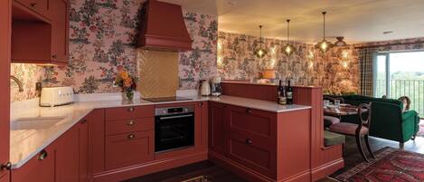 A kitchen with a built-in oven, a sink, and a dining area with a green sofa and a patterned rug.