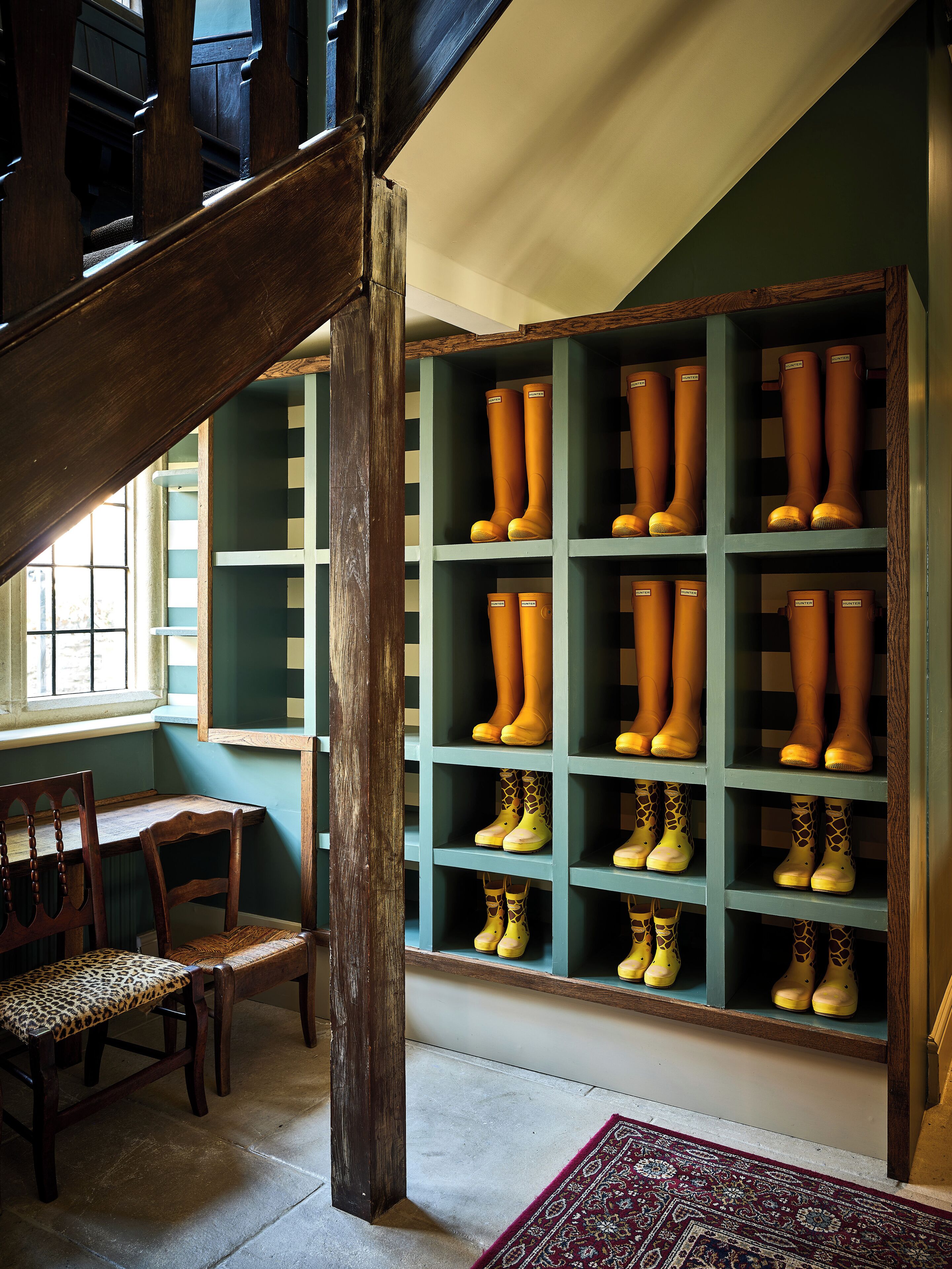 A room with a wooden staircase, a wooden chair, and a shelf with boots.