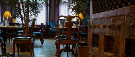 Un restaurante con mobiliario de madera, sillas tapizadas de verde y un separador decorativo de madera.