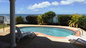 A pool area with lounge chairs and a view of the ocean.