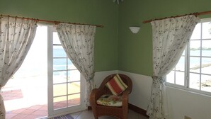 A room with a wicker chair, green walls, and a view of the sea through a large window.